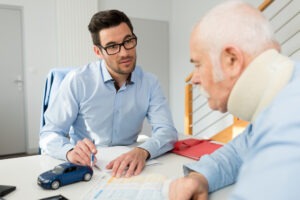 A man in a light blue shirt is talking to an older gentleman wearing a neck brace.