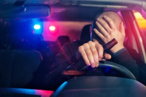 Un conductor ebrio cubriendo su cara en su automóvil. Llame a un abogado de accidentes de conducir bajo la influencia en Albuquerque si ha sido víctima de un conductor ebrio.