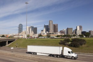 An 18 wheeler on the freeway with the dallas skyline in the background